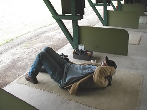 Image of a man wearing a black hat and glasses laying on his back while shooting a big bore silhouette