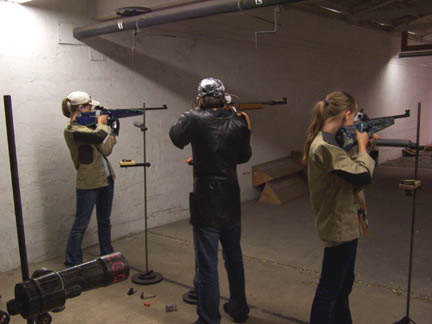 Image of three teenagers standing up while aiming small bore rifles indoors.